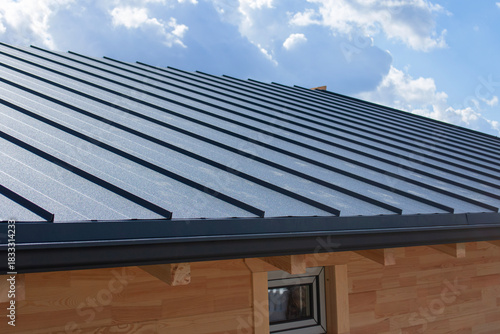 Dark gray standing seam metal roof and black gutter system on a building with natural wooden log walls for exterior building materials. Residential construction and home improvement.