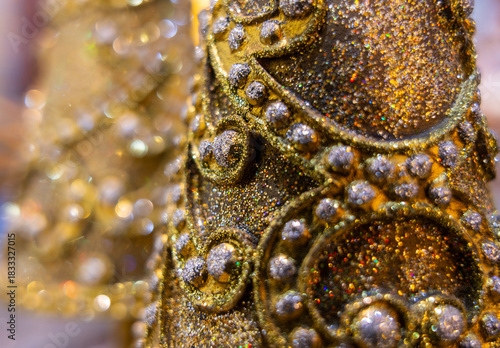 Christmas tree decoration closeup in gold, sparkles and another tree in bokeh background.