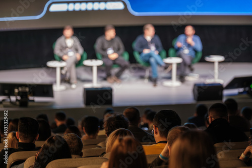 Panel discussion on stage with four speakers engaging audience during conference, capturing collaboration, learning, and networking in a large auditorium