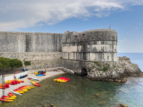 Fototapeta Naklejka Na Ścianę i Meble -  Colorful kayaks line the pebble beach beneath Dubrovnik's ancient stone walls and Fort Bokar, ready for an Adriatic adventure under a sunny Croatian sky.