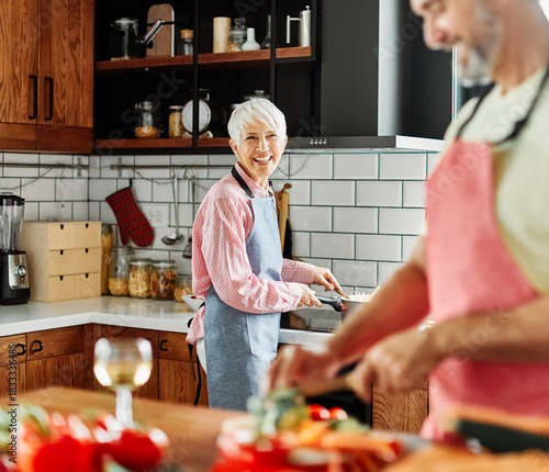 Portrait of happy senior mid aged mature couple prepering meal with fresh vegatebles in kitchen at hpme