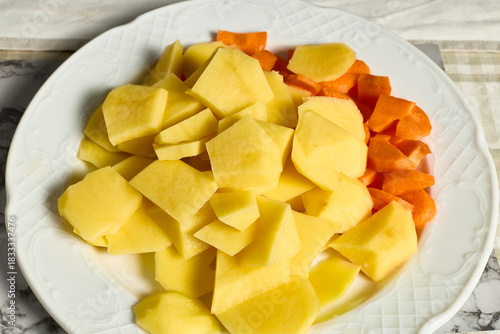 Potatoes and carrots. Kitchen table with a plate of potatoes and carrots cut into small pieces for making a soup recipe.