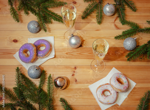 Glazed donuts, glasses of champagne, christmas balls and fir branches. Top view.