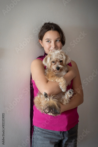 Fotografie Young girl standing against a wall and tenderly holding her small, fluffy dog in her arms