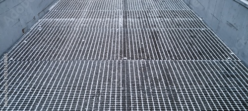Grate surface in industrial setting showcases flooring design and open spaces for water drainage during daytime