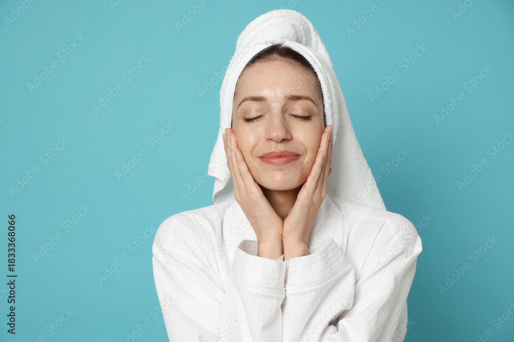 Obraz premium Woman wearing bathrobe with hair wrapped in towel on light blue background