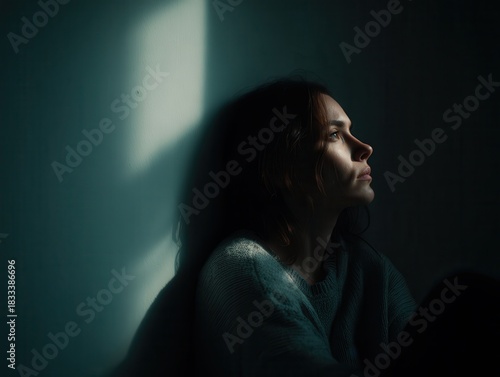 Portrait of a woman sitting in a dimly lit room, looking away toward a window