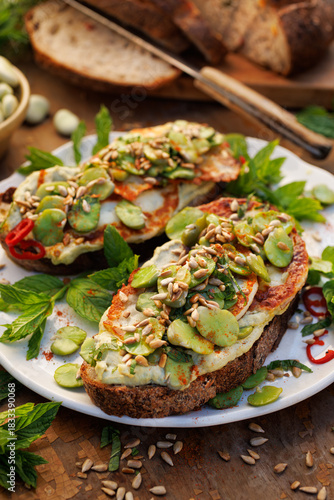 Broad bean spread sandwiches with and grilled goat cheese sprinkled with roasted sunflower seeds and fresh mint on a ceramic plate, close-up 