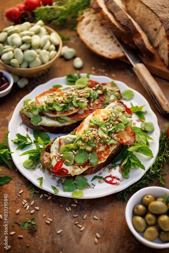 Broad bean spread sandwiches with and grilled goat cheese sprinkled with roasted sunflower seeds and fresh mint on a ceramic plate,  top view