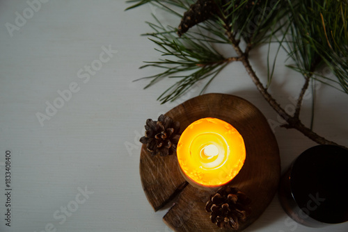 Burning candle fire on a wooden candlestick near green Christmas fir tree branch. Closeup ornament holiday background design concept with white empty copy space. Flat top view. Natural day light