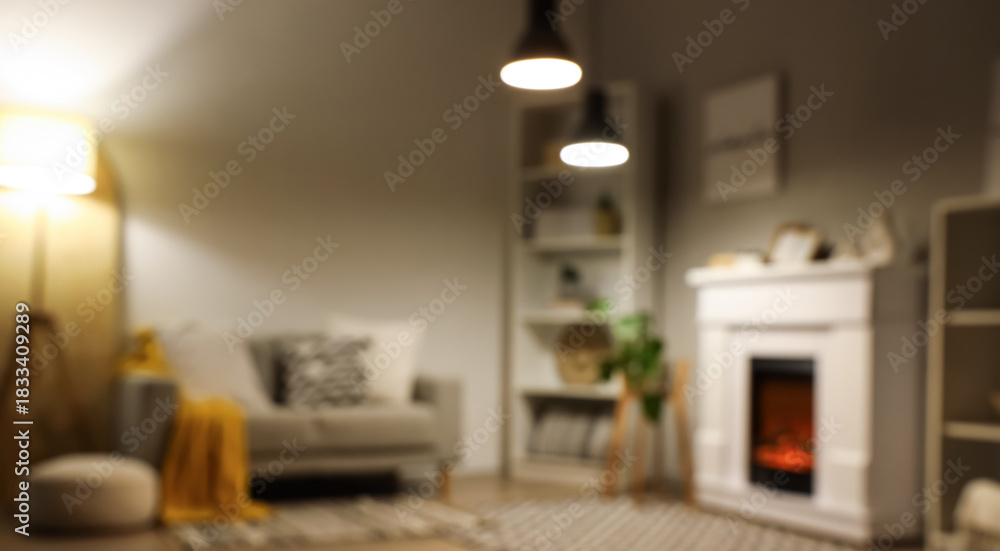 Fototapeta premium Blurred view of living room with fireplace, sofa and glowing lamps in evening