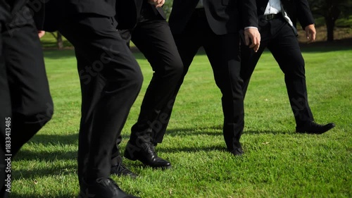 Group of men in a black pants and shoes walking on the green lawn grass in the park