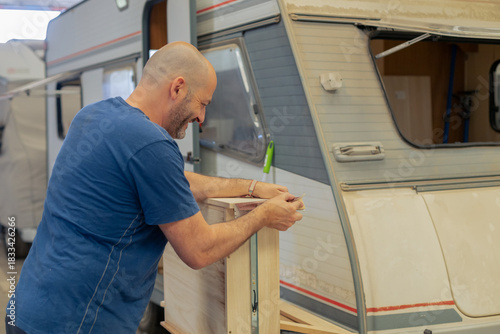 A young craftsman restores a caravan in a hangar.