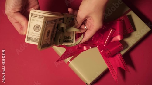 Gift box and stack of dollars on red background, representing cash gifts for Christmas, New Year, Valentines Day, celebrations, personal finance, gifting, savings and special holiday events