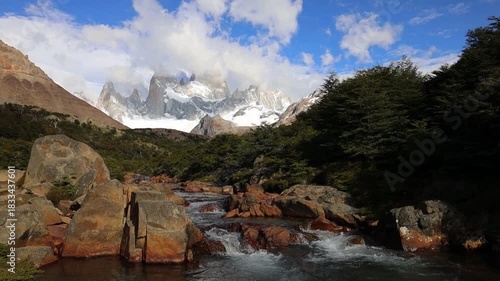 Fitzroy mountain in Patagonia with sharp granite peaks rugged terrain drifting clouds clear sky remote wilderness glacial valley rocky landscape natural environment and panoramic daylight view scenery
