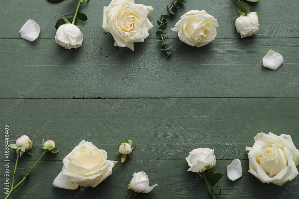 Naklejka premium Frame made of beautiful white roses and eucalyptus branch on green wooden background