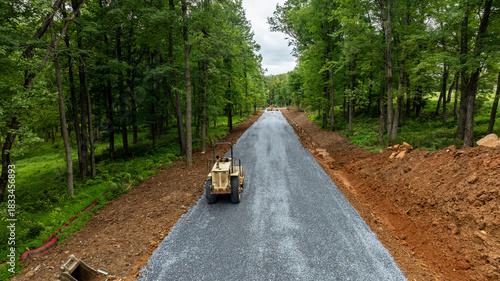 Construction workers are building a new road through a wooded area. The project aims to enhance access for residents and improve transportation in the region. Heavy machinery is visible in the scene.