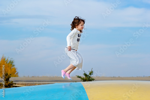 Girl is jumping on a bouncing pillow trampoline in the fall park.
