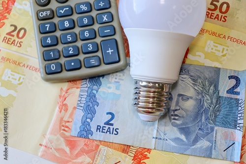 Conta de Luz (electricity bill in Portuguese) post-it reminder stuck on a light bulb, Brazilian Real banknotes and calculator. Electricity bill in Brazil concept.