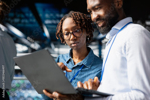 Supervisor and employee oversee performance outputs on server rigs for AI processing tasks. Server room specialists managing machine learning automation to ensure workflow, neural network.