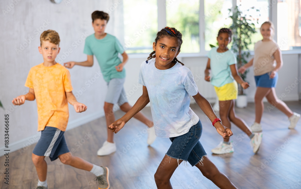 Fototapeta premium Positive boy exercising in group of classmates during dance class at school