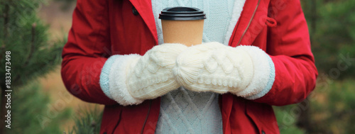 Close up female hand holding cup of hot coffee drink against Christmas tree in winter forest