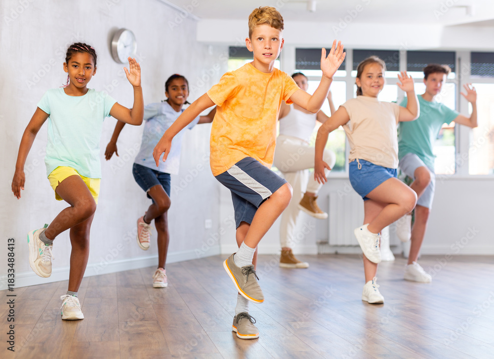 Fototapeta premium Cheerful tween boy having fun while training movements of modern group dance in children choreography class ..