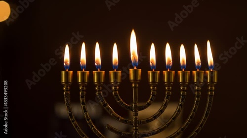 Nine lit oil lamps on an ornate brass menorah against a dark background