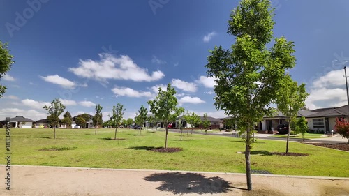 A newly landscaped suburban park in Tarneit, Melbourne, Australia, featuring young trees planted across a wide green open space with modern houses bordering the reserve. Peaceful living environment