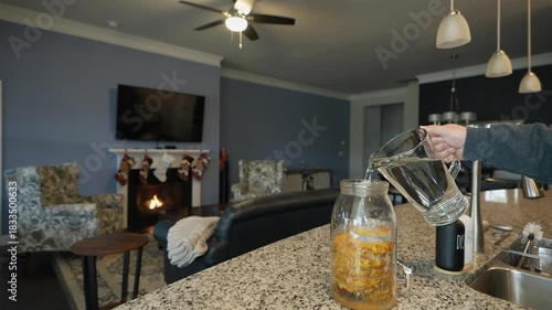 pouring water from pitcher into jar of fermenting tepache