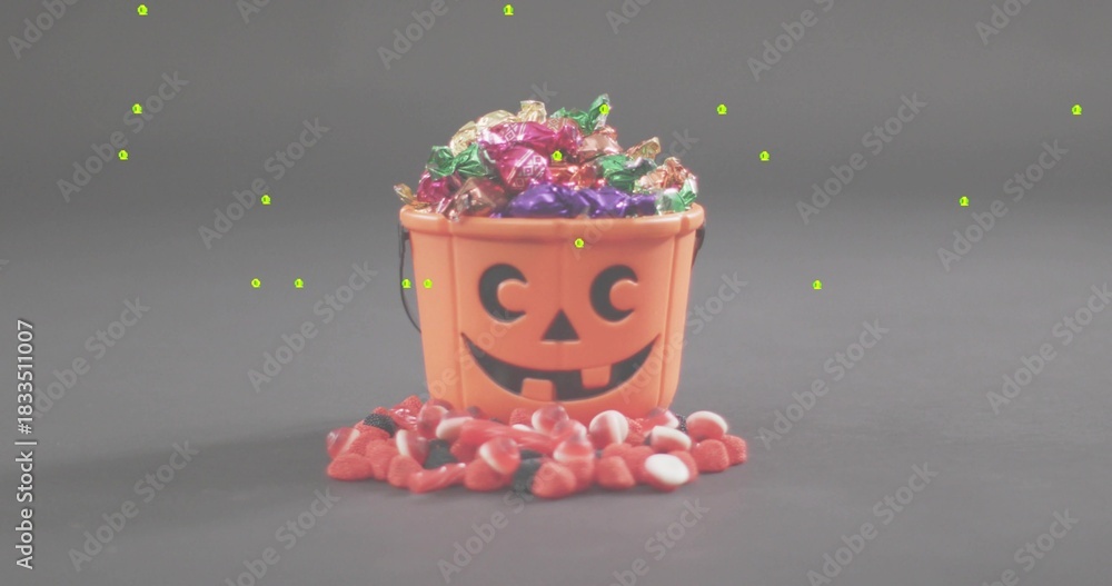 Fototapeta premium Displaying orange pumpkin bucket spilling foil candies and red-and-white sweets on gray tabletop