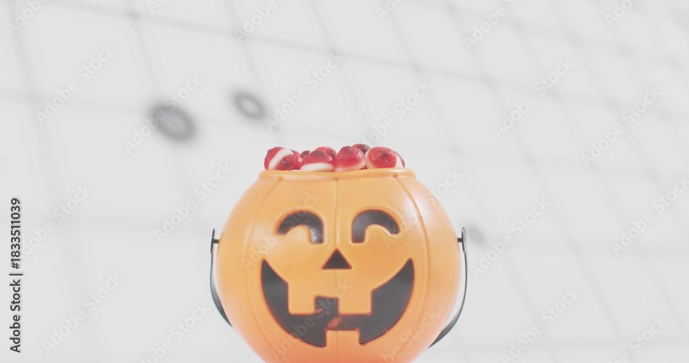 Naklejka premium Showing orange pumpkin bucket with face, black handle spilling red candies under ceiling grid