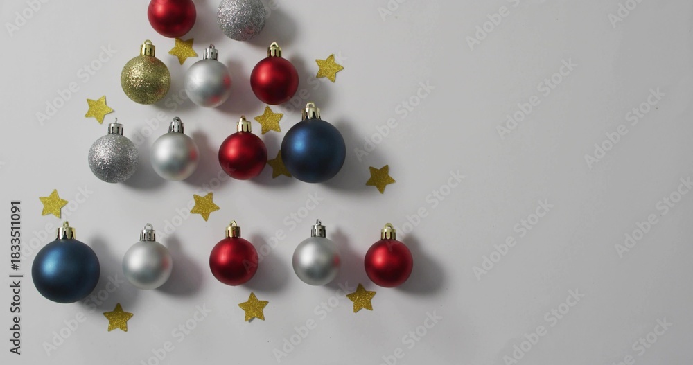 Fototapeta premium Displaying triangular red silver blue gold baubles with metal caps on white tabletop, copy space