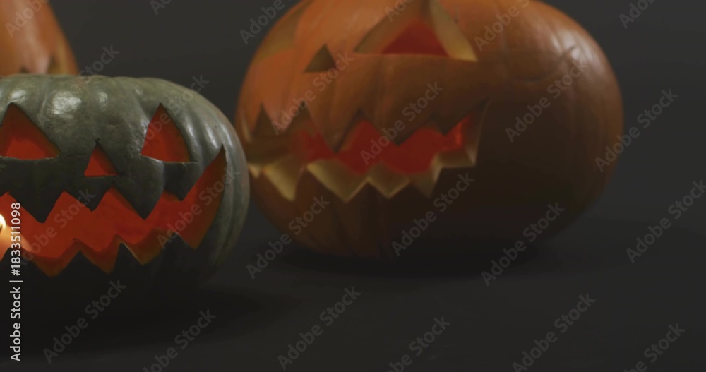 Fototapeta premium Glowing pair of carved jack-o'-lantern pumpkins casting warm light, showing internal glow in studio