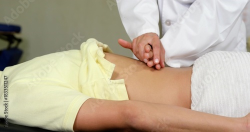 Examining patient torso, doctor in white coat palpating abdomen on table, yellow top being lifted