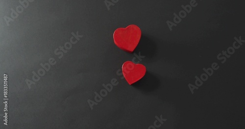 Displaying two red heart blocks resting on dark matte surface, casting soft shadows, copy space