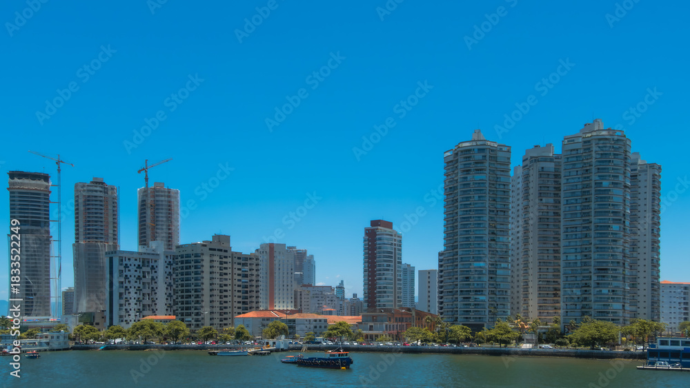 Fototapeta premium City skyline with modern skyscrapers and construction cranes reflecting urban development over the blue waterfront on a sunny day
