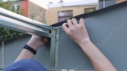 One guy attaches braces to the roof of a metal shed with a screwdriver.