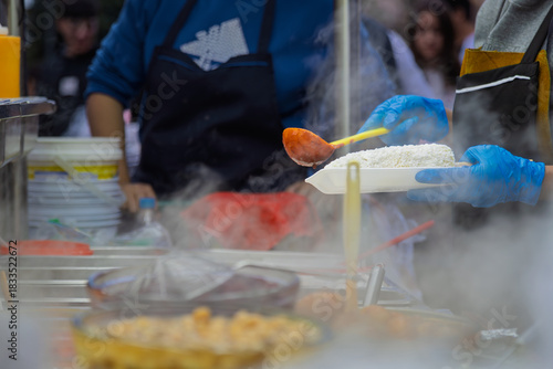 Vendor prepares Mexican corn topped with cheese and chili sauce at night food stall in Guadalajara, Mexico