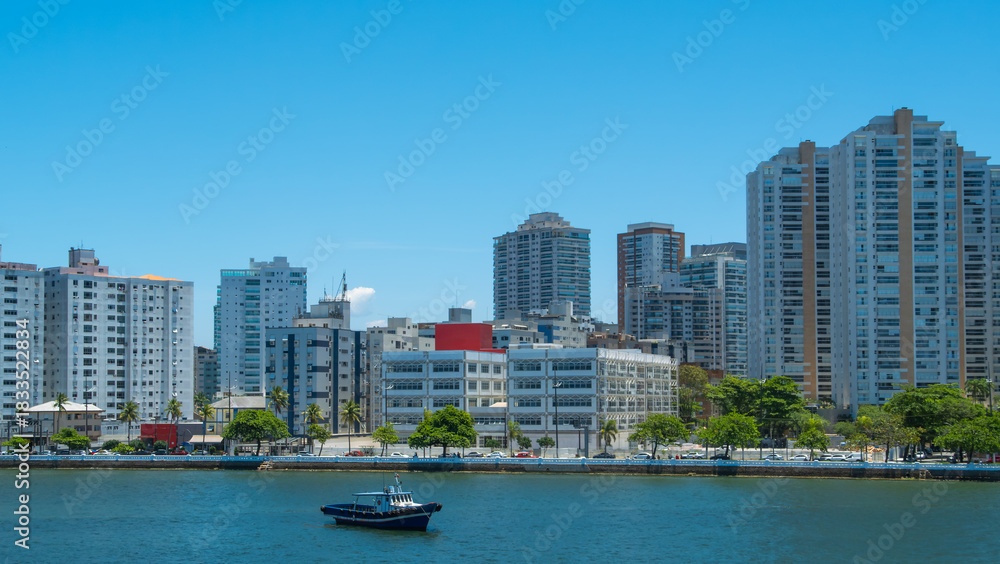Naklejka premium Coastal city with a dense skyline of modern high-rise buildings and skyscrapers overlooking the water, with a small boat in the foreground