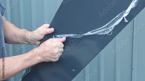 The hands of a mature Caucasian man remove a thin film from a triangular part of a profile shed.