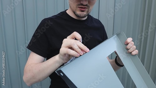 A cheerful worker removes a thin film from a triangular part of a profile shed.