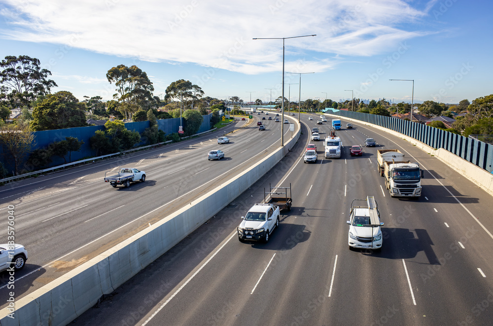 Fototapeta premium Princes Freeway at Laverton North in Melbourne, Australia, showing multi-lane traffic. Wide divided highway with sound barriers, concrete median. Concept of commuting, road infrastructure