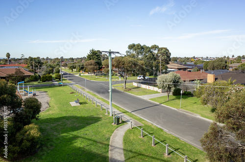 Fototapeta Naklejka Na Ścianę i Meble -  Elevated view of a quiet suburban street in Altona Meadows, Melbourne, Australia, featuring open green space, a small playground, residential houses. A peaceful, clean neighborhood with utility poles