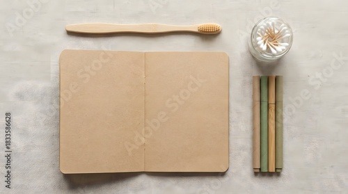 Top-down flat-lay of bamboo and recycled products including toothbrush, notebook and pens on neutral surface. Clean minimalist eco arrangement with negative space.