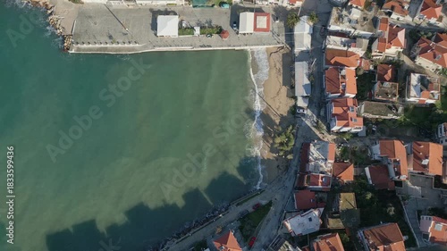 Aerial drone view of a traditional coastal village on Thassos island in Greece. Sunlight reflecting on the sea, dense hillside houses and clear Mediterranean shoreline