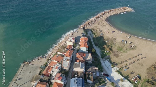 Aerial drone view of a traditional coastal village on Thassos island in Greece. Sunlight reflecting on the sea, dense hillside houses and clear Mediterranean shoreline