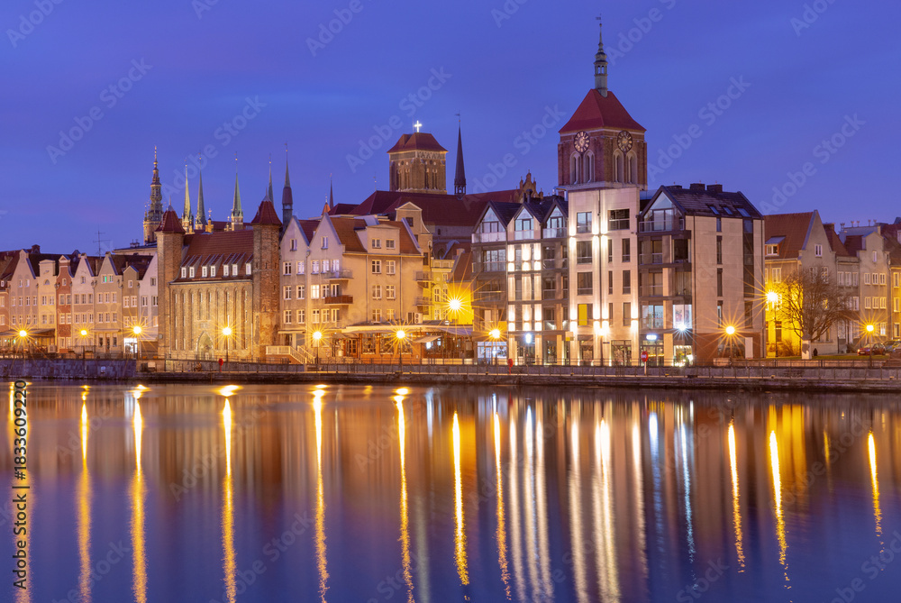 Fototapeta premium Historic waterfront houses and illuminated church towers in the old town of Gdansk Poland at night