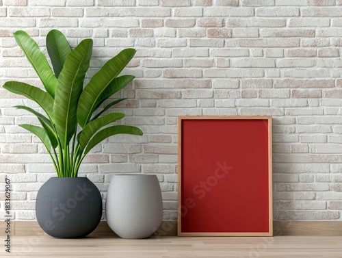 A large green plant in a dark gray pot, a white pot and a red frame lean against a white brick wall in a modern interior.