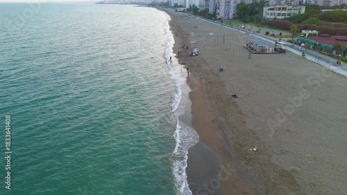 Mersin, Turkey. Beach with people and cafe in residential area with apartment buildings. Aerial view of coastal social life in Mezitli.. Aerial View